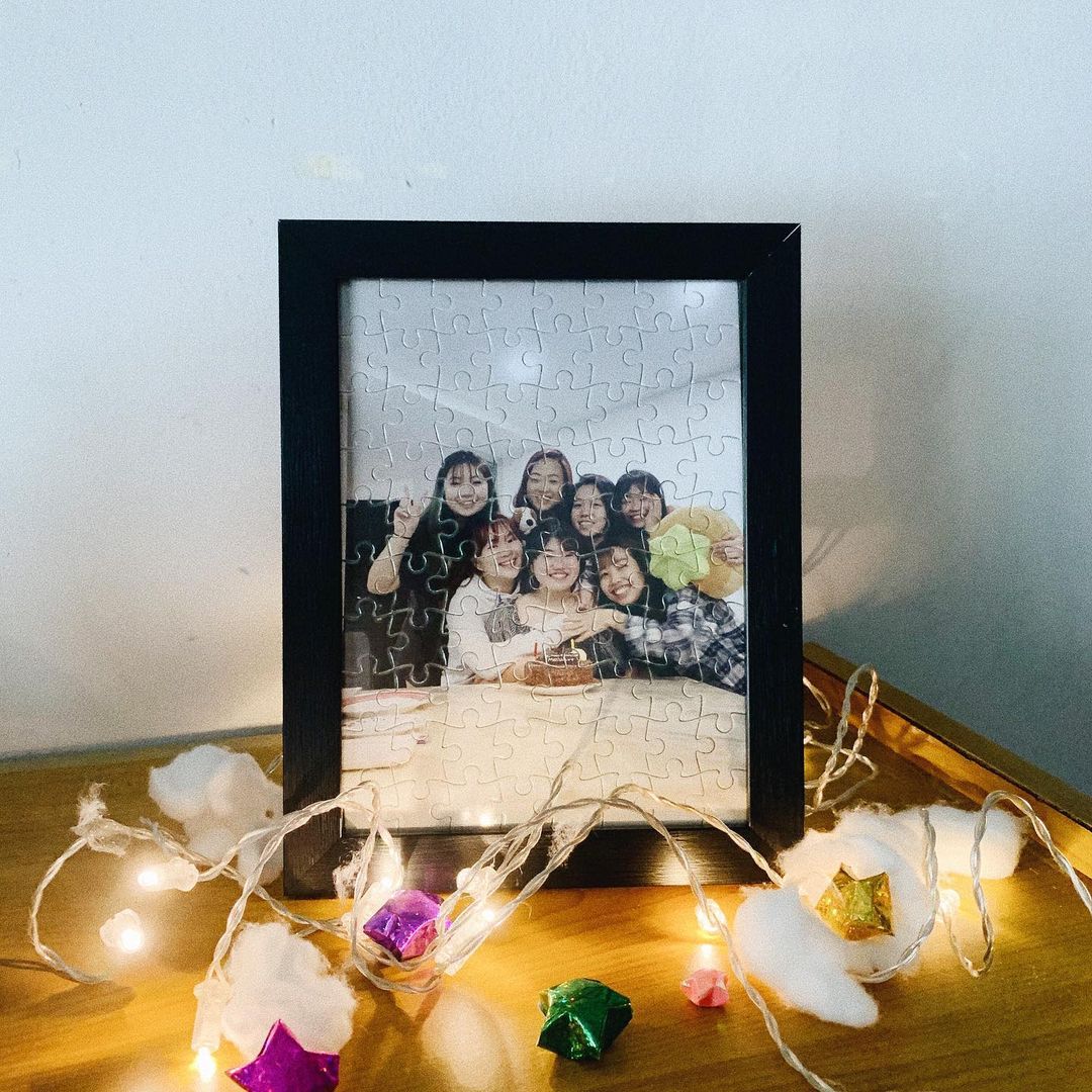 Custom photo jigsaw puzzle in a black frame, displayed on a shelf with fairy lights
